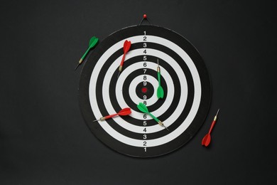 Photo of Dart board and colorful arrows on black background, flat lay