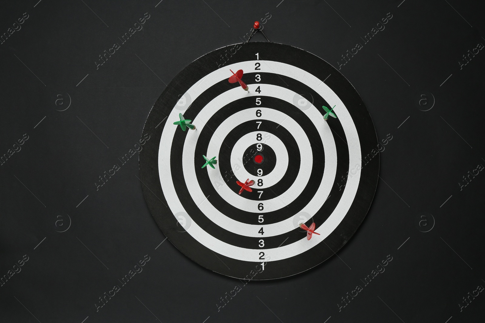 Photo of Dart board with colorful arrows hanging on black wall