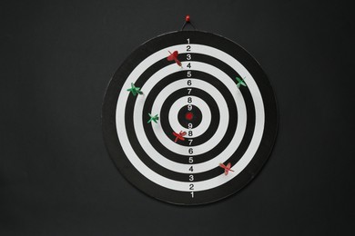 Photo of Dart board with colorful arrows hanging on black wall