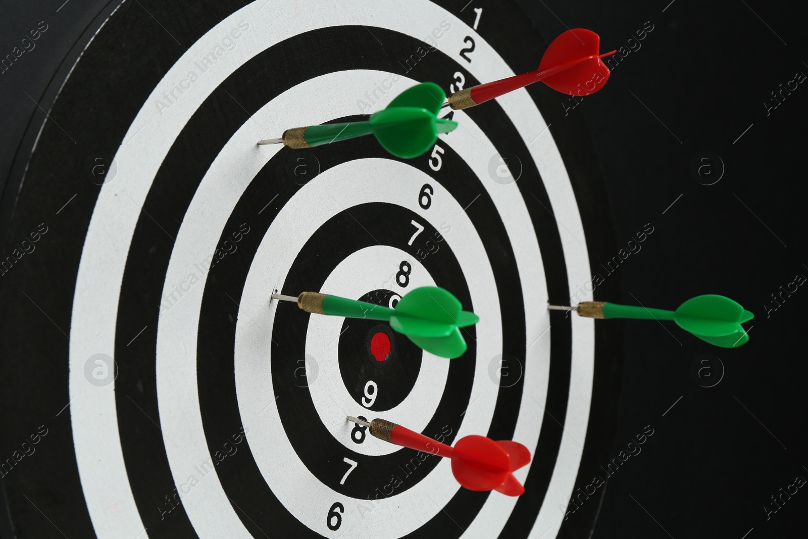 Photo of Dart board with colorful arrows hanging on black wall, closeup