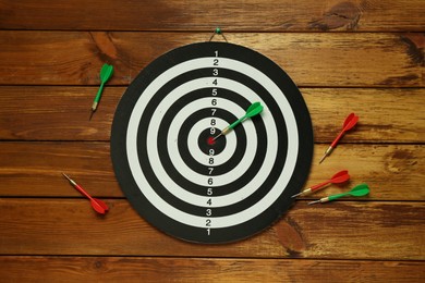 Photo of Dart board and colorful arrows on wooden background, flat lay