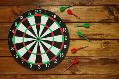 Photo of Dart board and colorful arrows on wooden background, flat lay