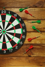 Photo of Dart board and colorful arrows on wooden background, flat lay