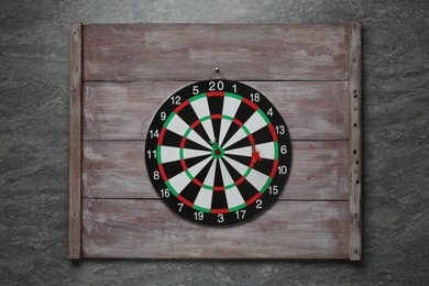 Photo of Dart board with colorful arrows and wooden planks hanging on grey wall