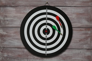 Photo of One dart board with colorful arrows on wooden rustic background, top view