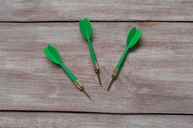 Photo of Green dart arrows on wooden rustic table, flat lay