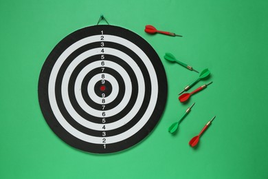 Photo of Dart board and colorful arrows on green background, flat lay