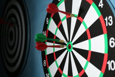 Photo of Dart board with colorful arrows hanging on blue wall, closeup