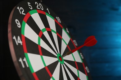 Photo of Dart board with red arrow against blurred blue background, closeup