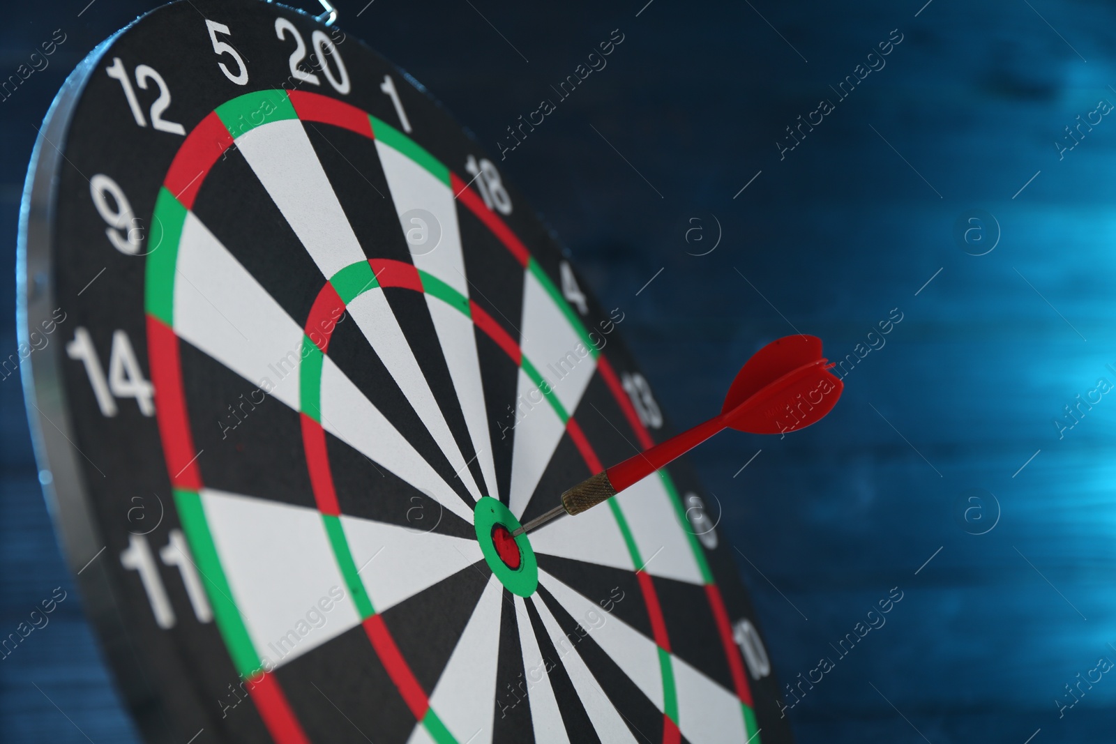 Photo of Dart board with red arrow against blurred blue background, closeup