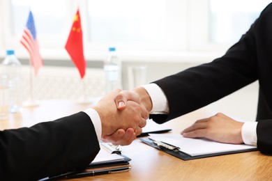 Photo of Diplomats shaking hands during meeting at wooden table indoors, closeup