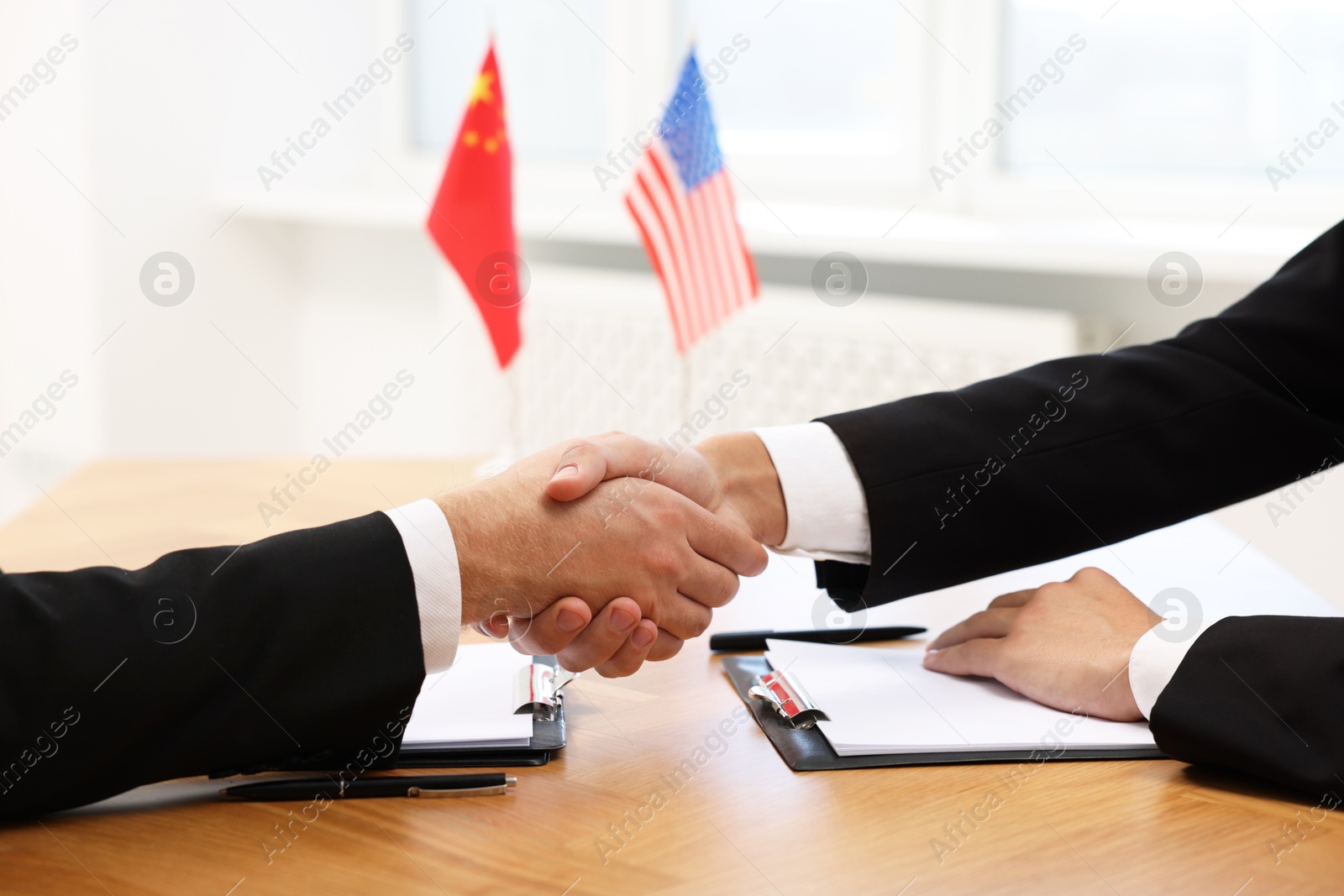 Photo of Diplomats shaking hands during meeting at wooden table indoors, closeup