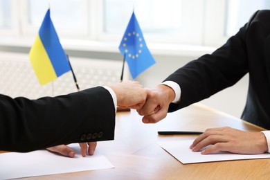 Photo of Diplomats shaking hands during meeting at wooden table indoors, closeup