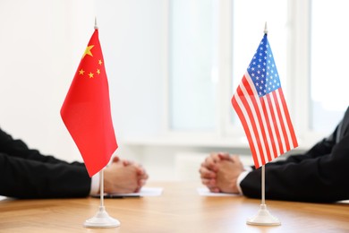 Photo of Diplomats negotiating during meeting at table indoors, focus on flags of USA and China