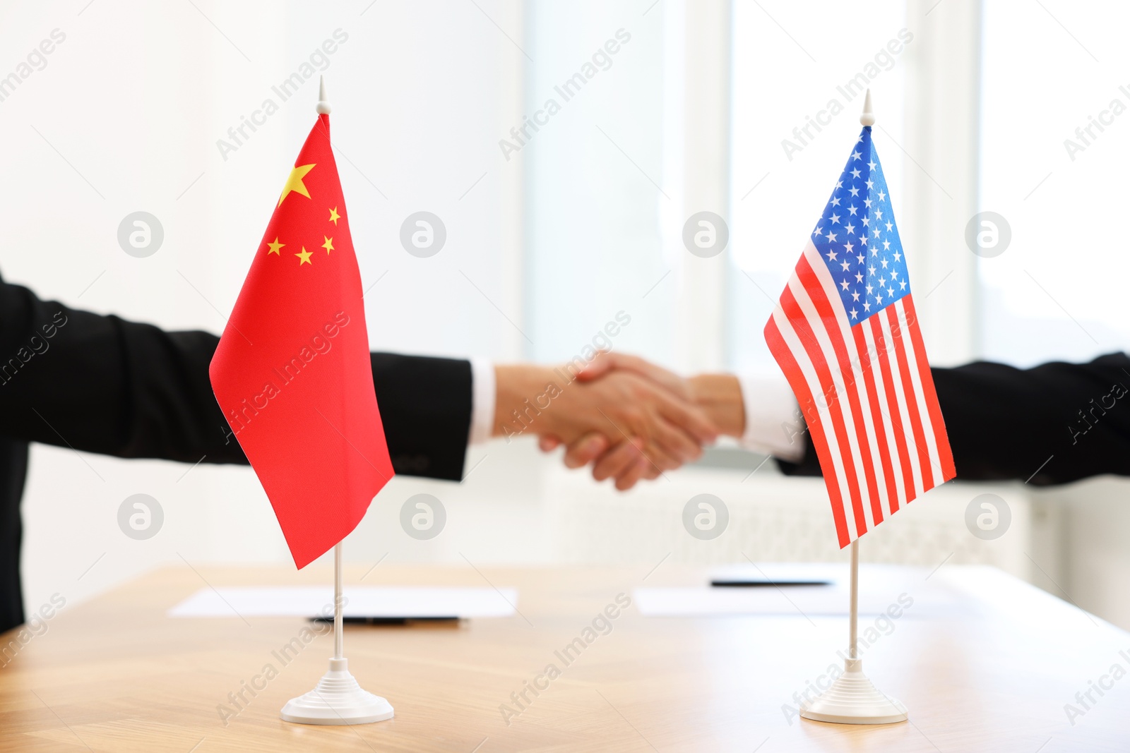 Photo of Diplomats shaking hands during meeting indoors, focus on flags of USA and China