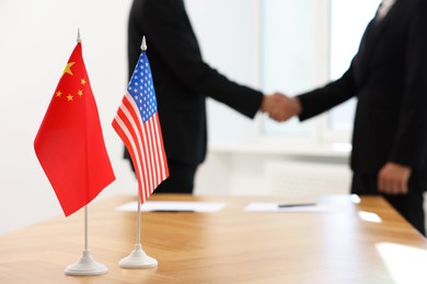 Photo of Diplomats shaking hands during meeting indoors, focus on flags of USA and China