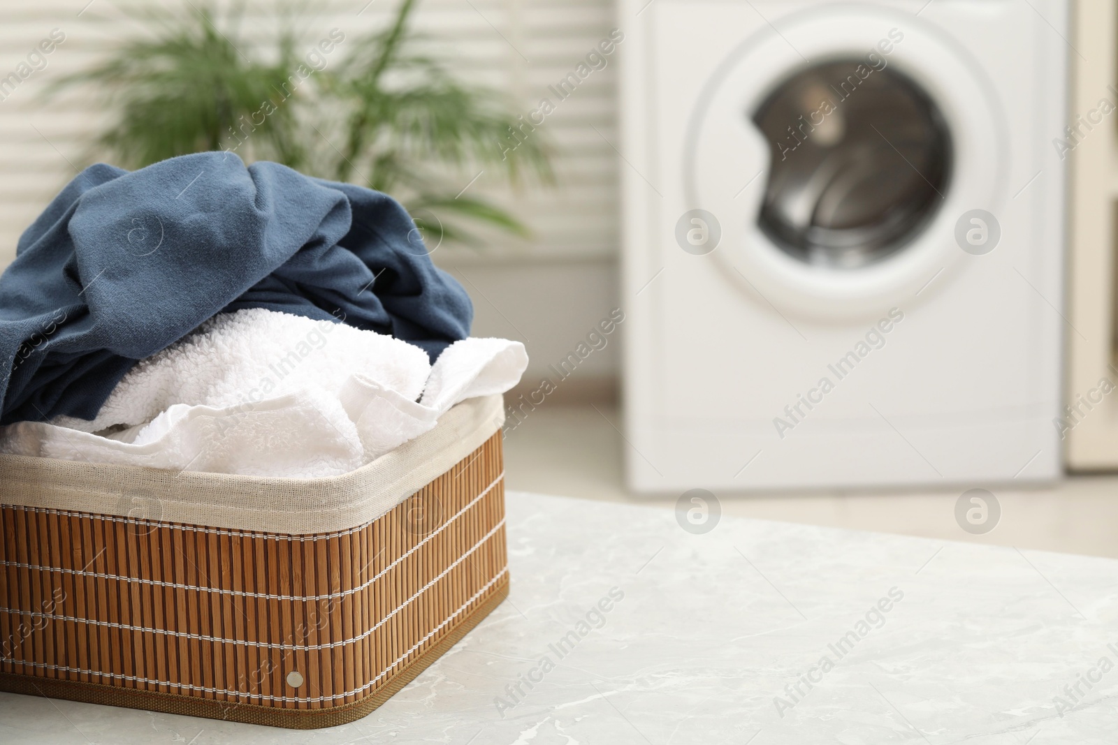 Photo of Wicker basket with laundry on light table in bathroom. Space for text