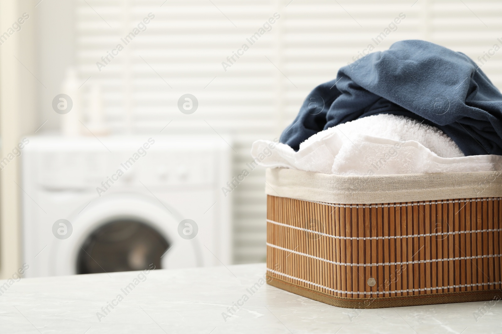 Photo of Wicker basket with laundry on light table in bathroom. Space for text