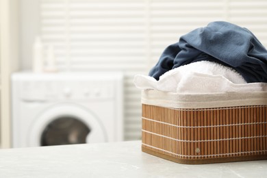 Photo of Wicker basket with laundry on light table in bathroom. Space for text