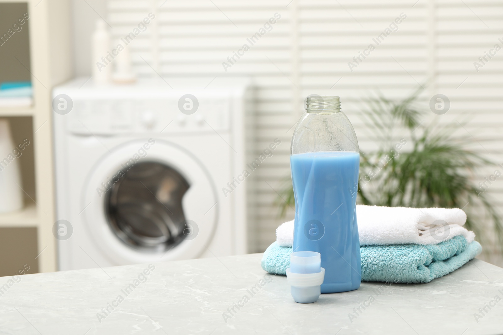 Photo of Laundry detergent and clean terry towels on light grey marble table in bathroom. Space for text