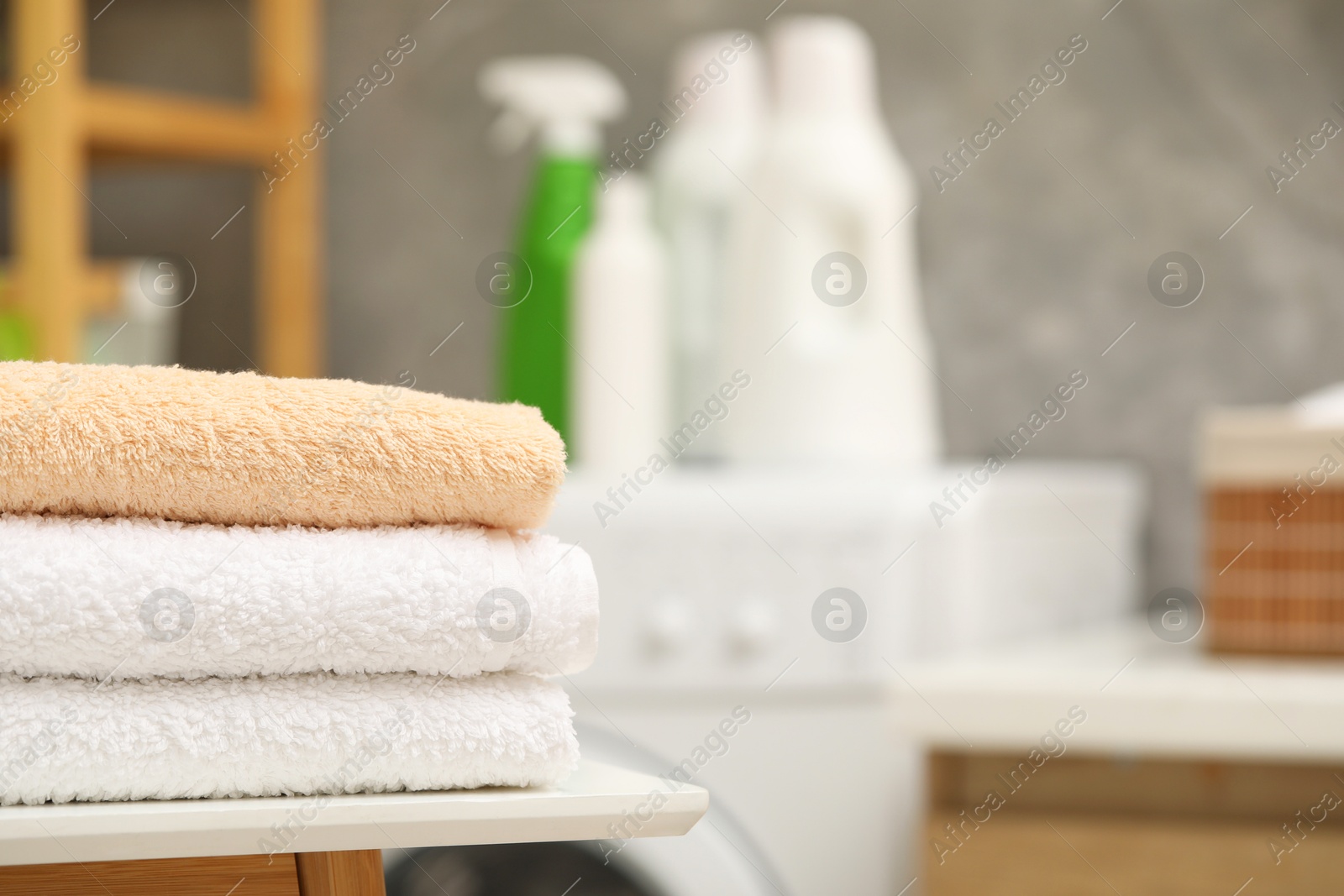 Photo of Stacked terry towels on white table in laundry room. Space for text