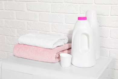 Photo of Laundry detergents, cap and stacked clean towels on washing machine in bathroom