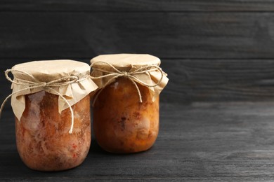 Photo of Canned meat in glass jars on wooden table, space for text