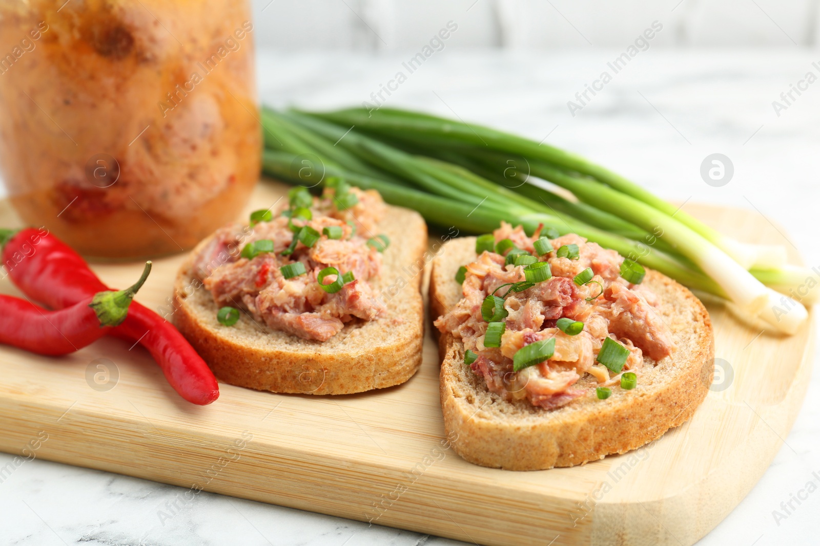 Photo of Sandwiches with canned meat, green onions and chili peppers on white marble table, closeup