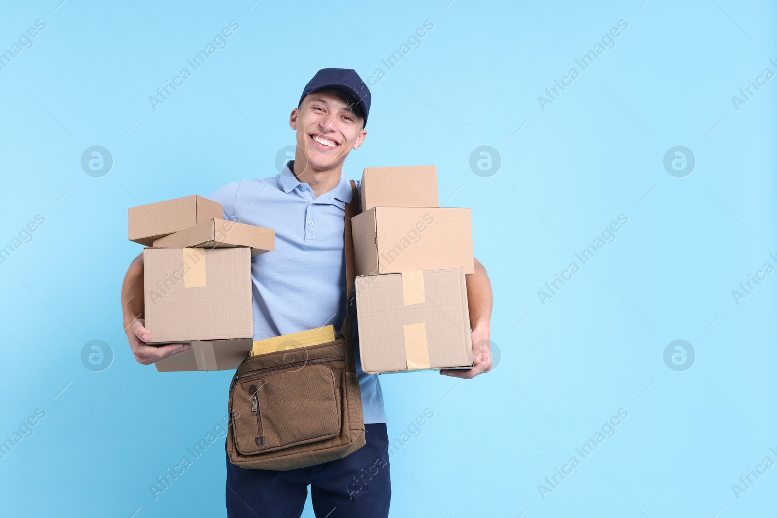 Photo of Happy postman with bag and parcels on light blue background. Space for text