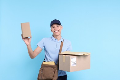 Photo of Happy postman with bag, envelopes and parcels on light blue background