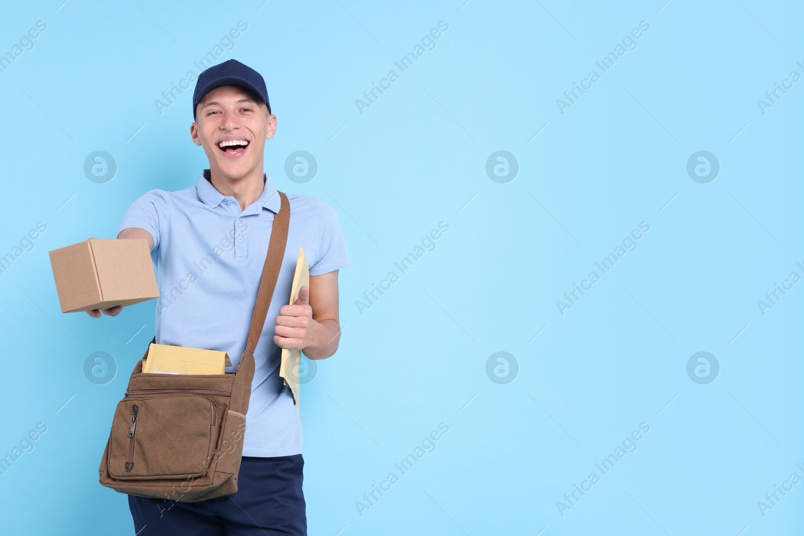 Photo of Happy postman with bag, envelopes and parcel on light blue background. Space for text