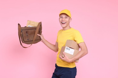 Photo of Happy postman with bag and parcels on pink background