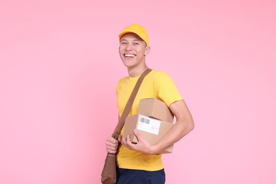 Photo of Happy postman with bag and parcels on pink background