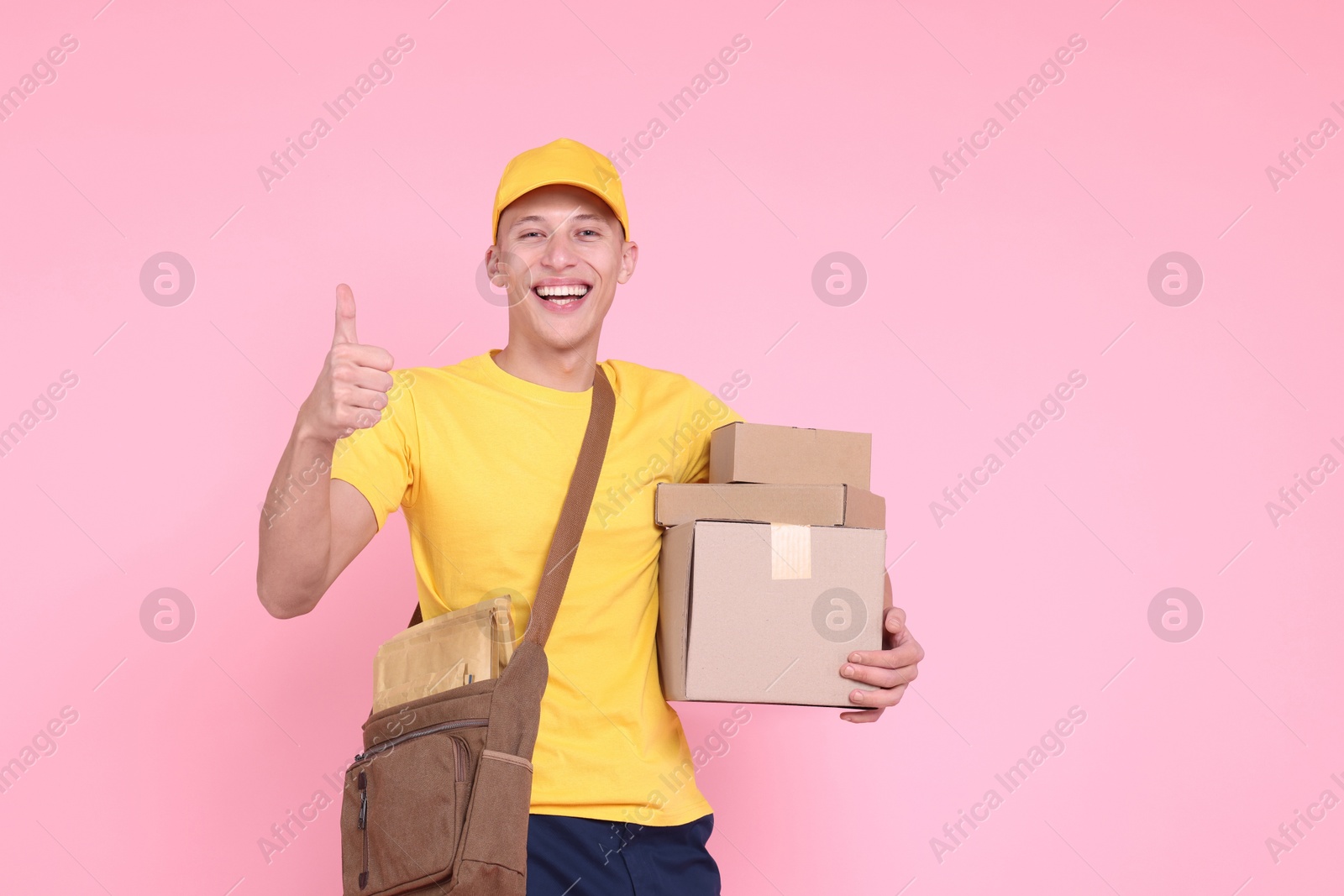 Photo of Happy postman with parcels showing thumbs up on pink background