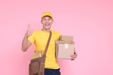 Happy postman with parcels showing thumbs up on pink background