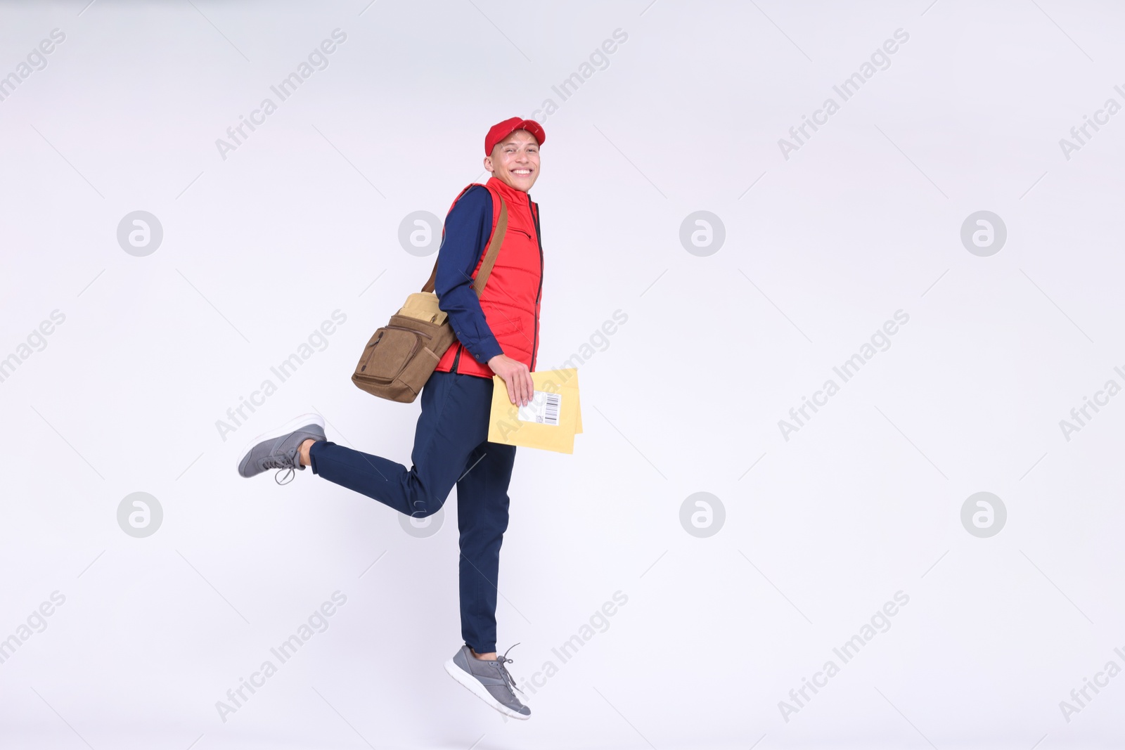 Photo of Happy postman with bag and envelopes jumping on white background