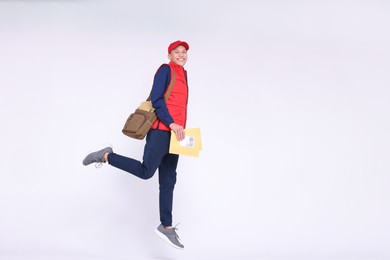 Photo of Happy postman with bag and envelopes jumping on white background