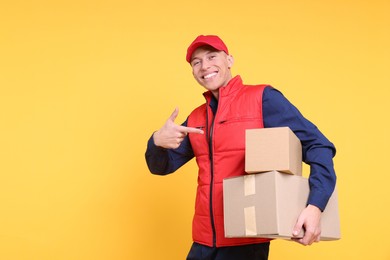 Photo of Happy postman pointing at parcels on yellow background. Space for text