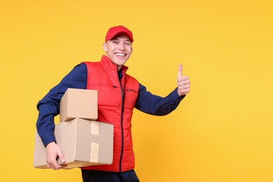 Photo of Happy postman with parcels showing thumbs up on yellow background. Space for text