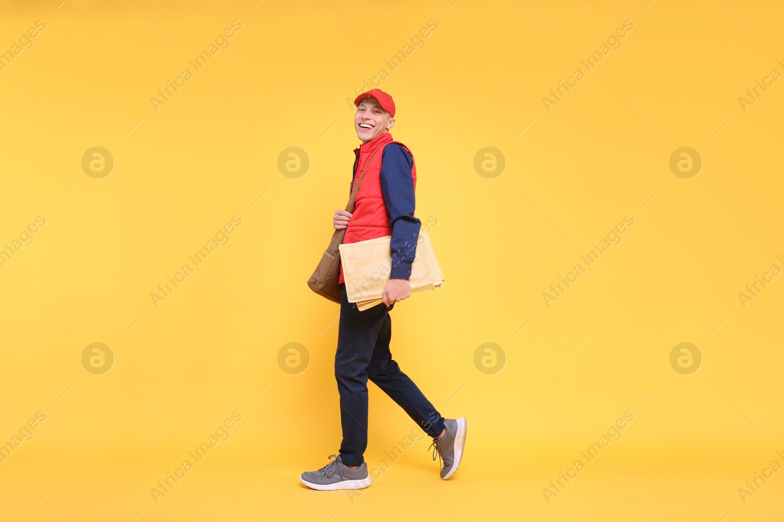 Photo of Happy postman with bag and envelopes on yellow background