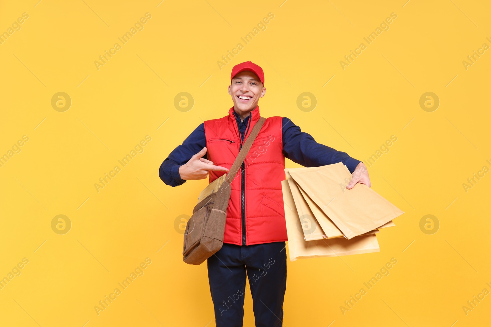 Photo of Happy postman with bag pointing at envelopes on yellow background