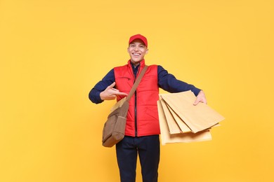 Photo of Happy postman with bag pointing at envelopes on yellow background