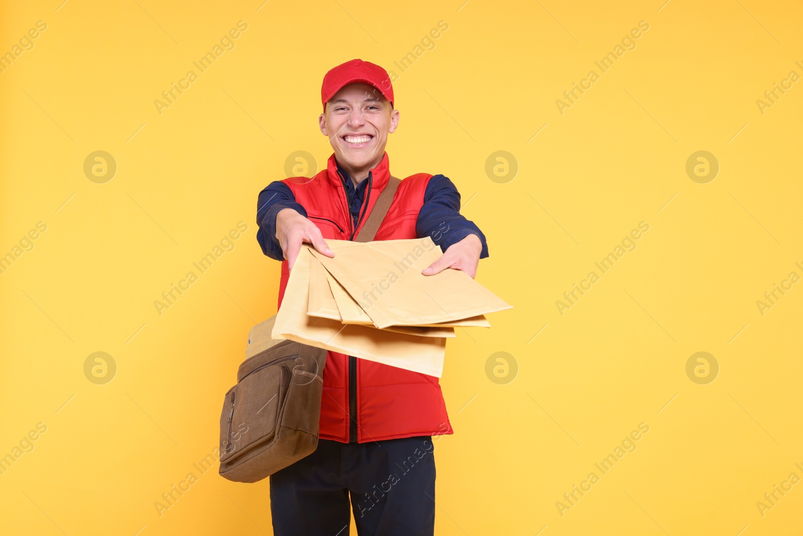 Photo of Happy postman with bag giving envelopes on yellow background