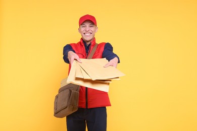 Photo of Happy postman with bag giving envelopes on yellow background