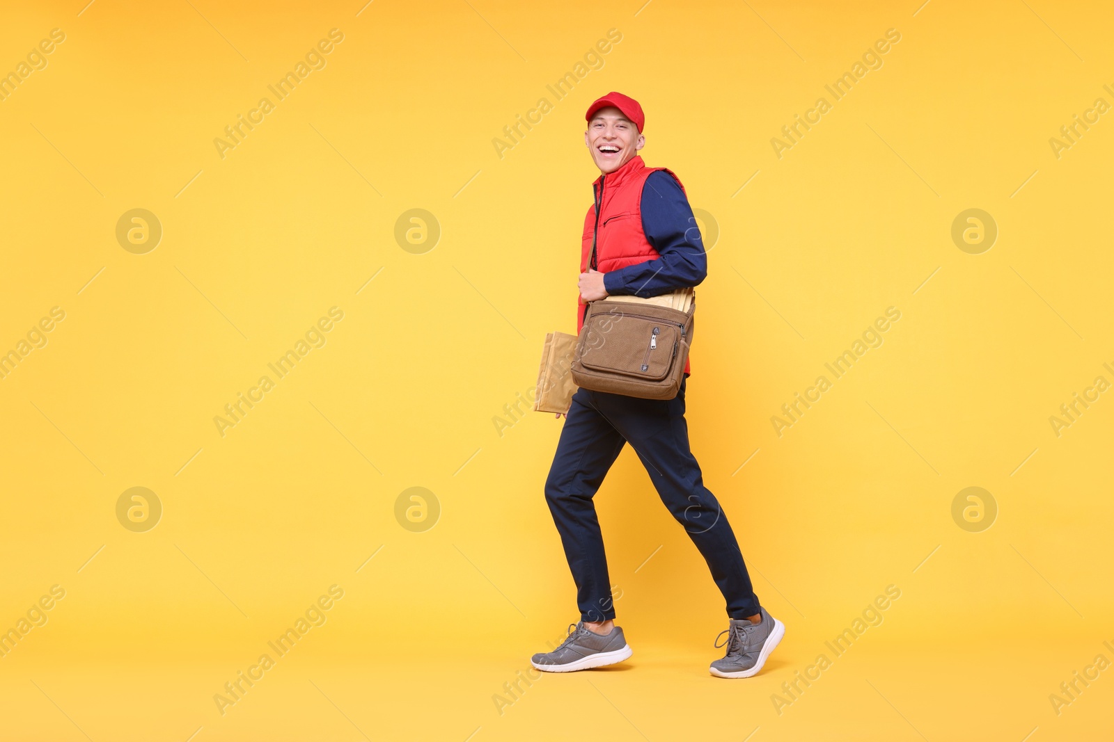 Photo of Happy postman with bag and envelopes on yellow background