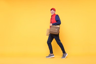 Happy postman with bag and envelopes on yellow background