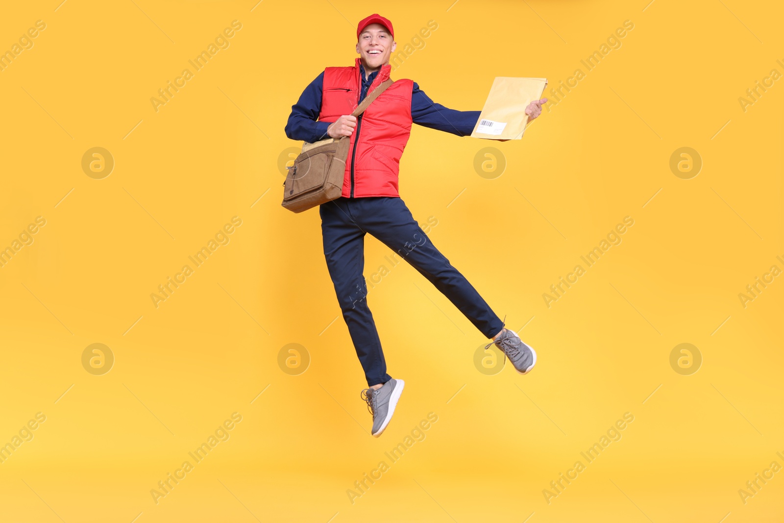 Photo of Happy postman with bag and envelopes jumping on yellow background