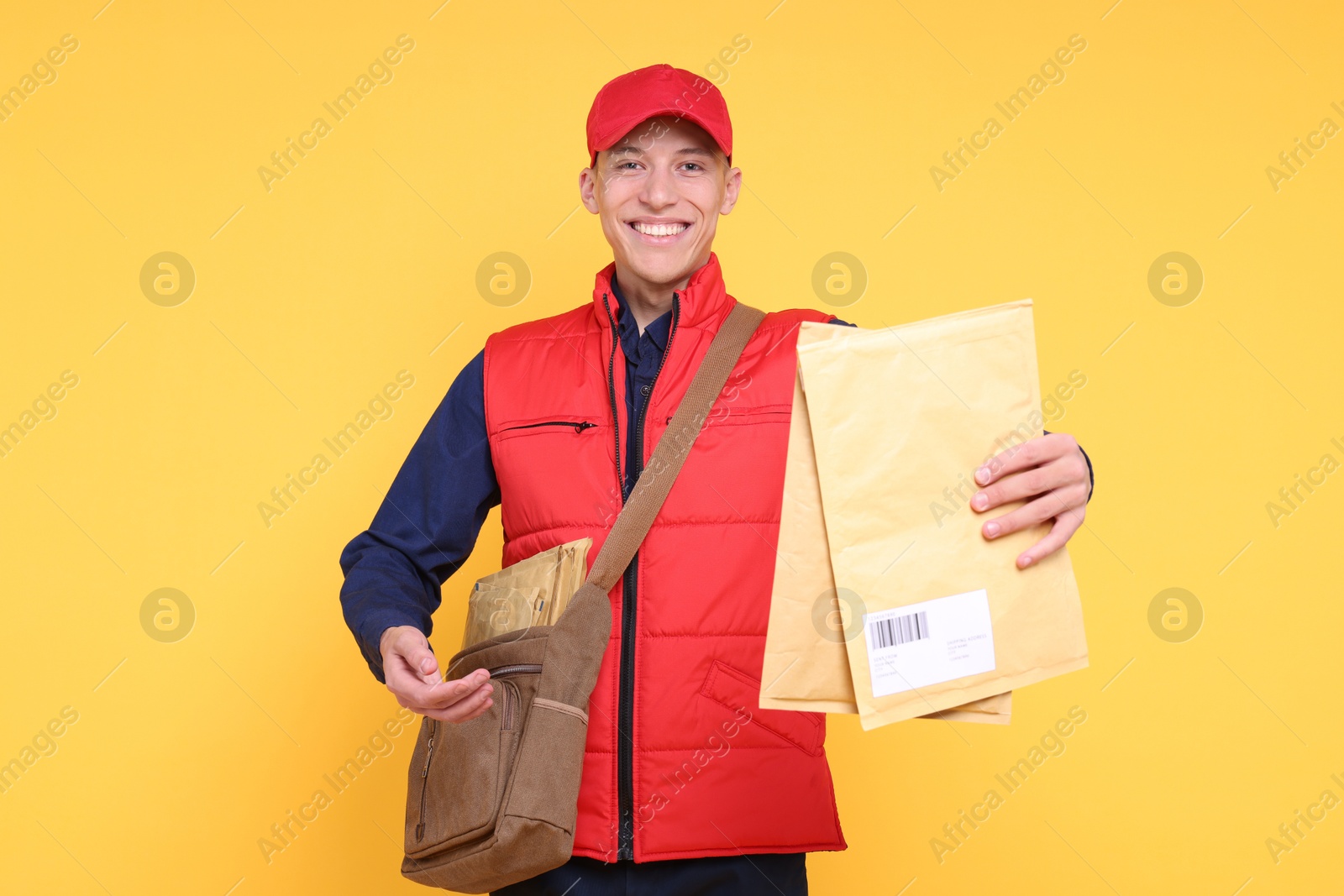 Photo of Happy postman with bag and envelopes on yellow background