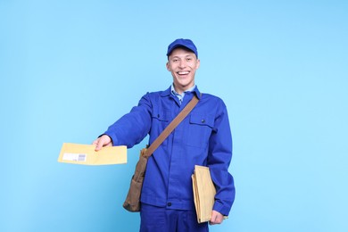 Photo of Happy postman with bag giving envelope on light blue background