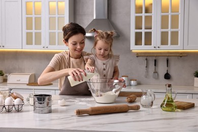 Photo of Smiling housewife cooking with her little daughter at marble table in kitchen